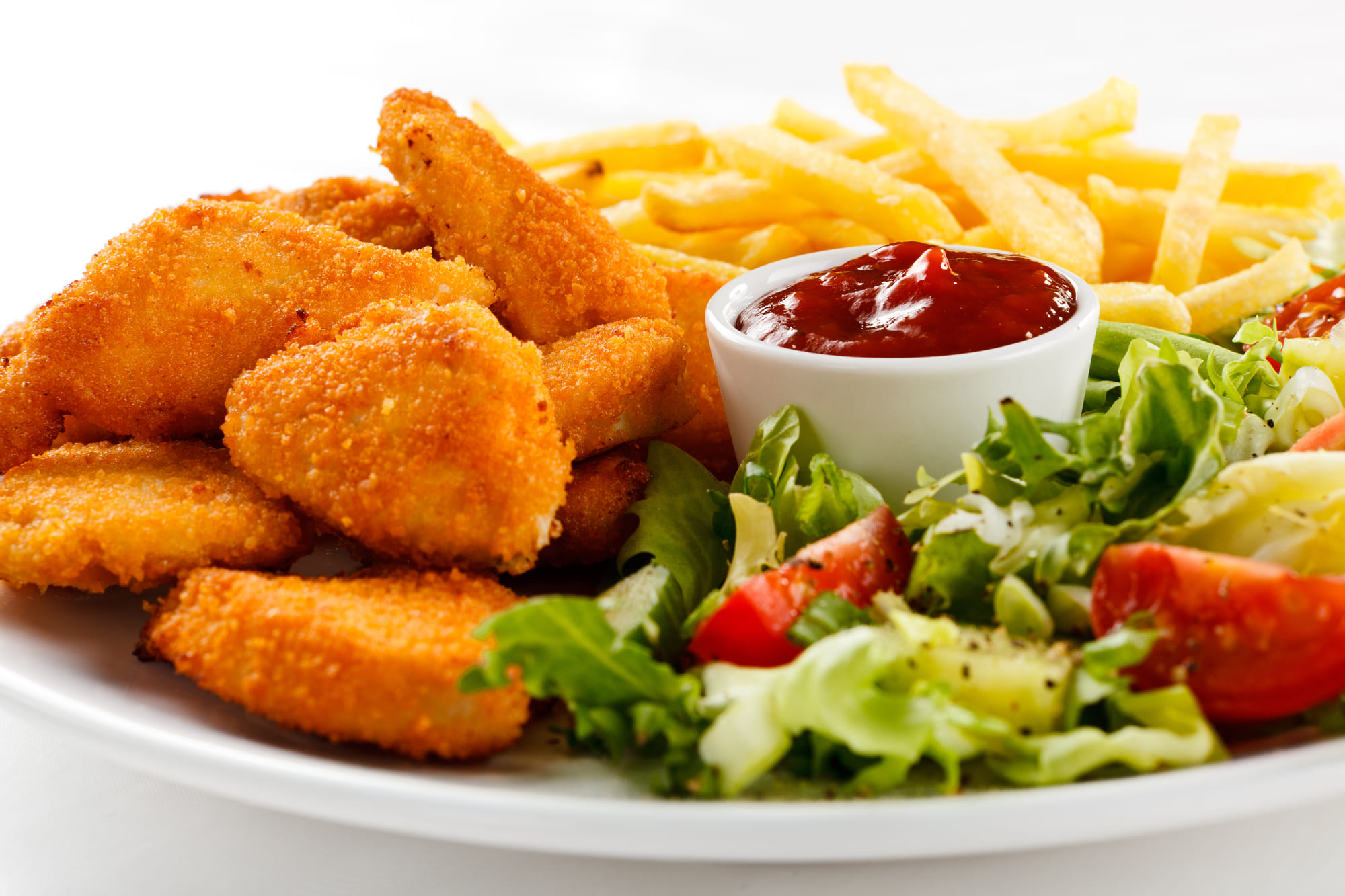 Teller mit panierten Hähnchenstreifen, Pommes Frites, einem Salat und einer Tasse Ketchup dazu.