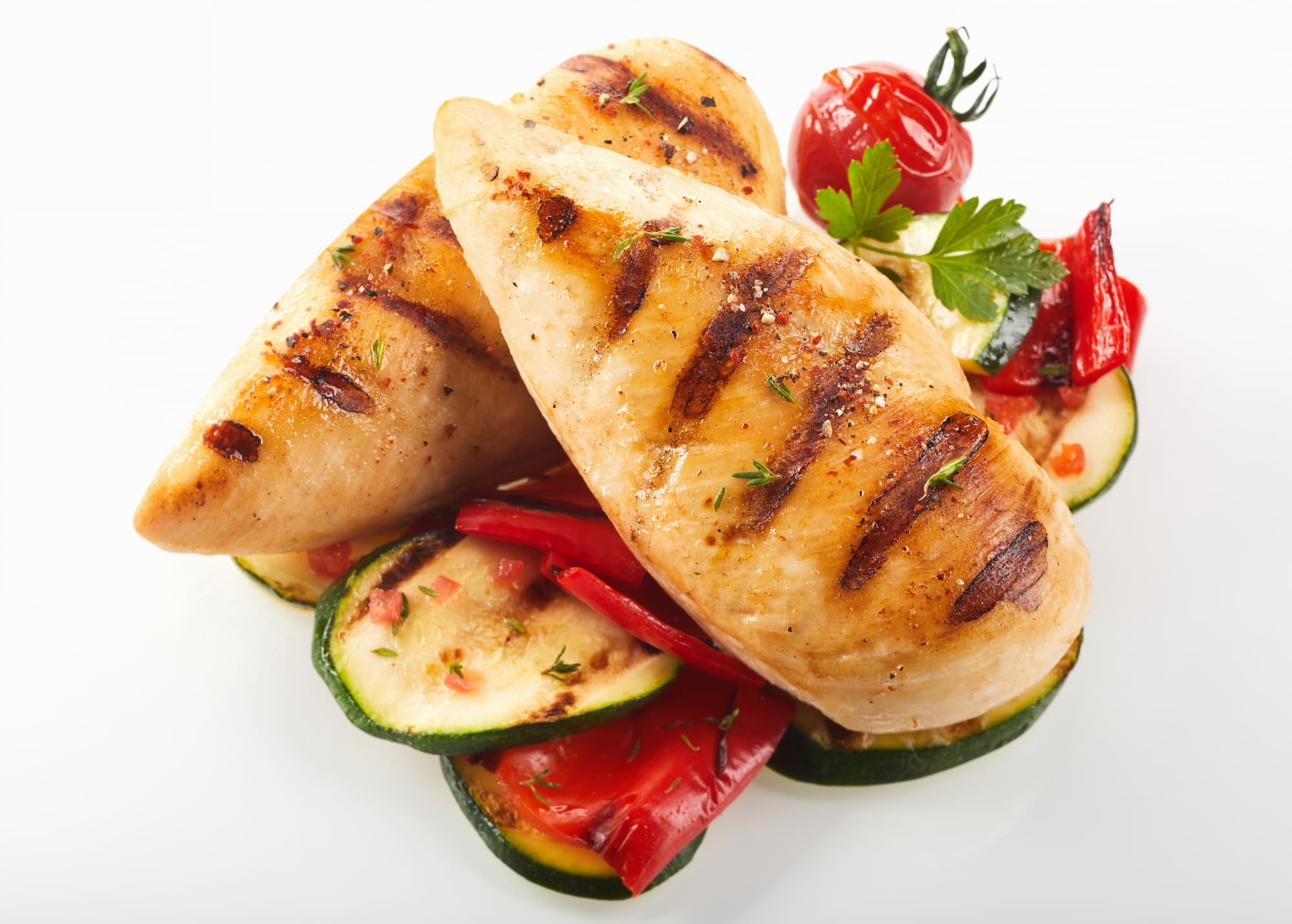 Gegrillte Hähnchenbrust, serviert mit Zucchini, roter Paprika und einer Kirschtomate auf einem weißen Teller.