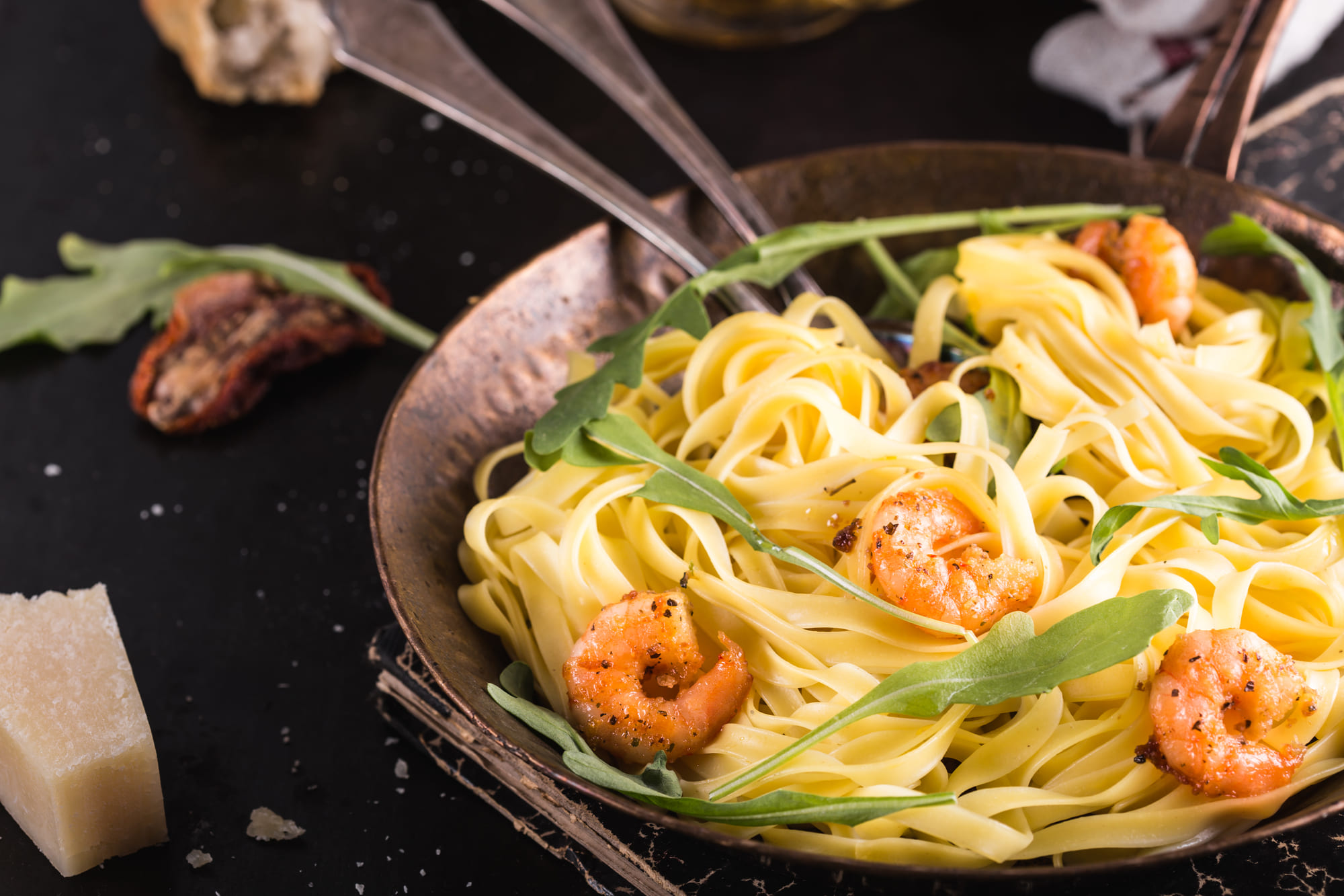 Ein Teller Fettuccine-Nudeln mit Garnelen und Rucola, serviert mit Käse und Brot als Beilage.