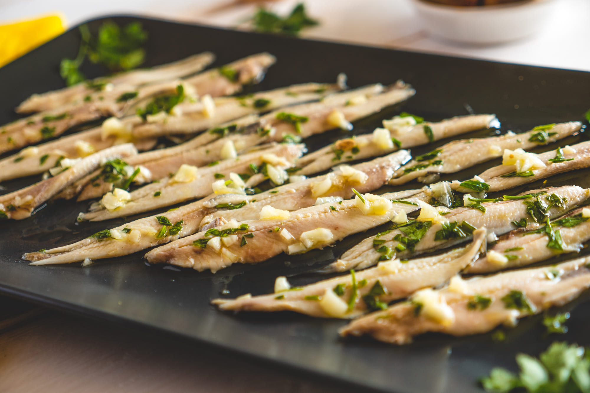 Filets von mariniertem Fisch, garniert mit gehacktem Knoblauch und Petersilie auf einem schwarzen Tablett.