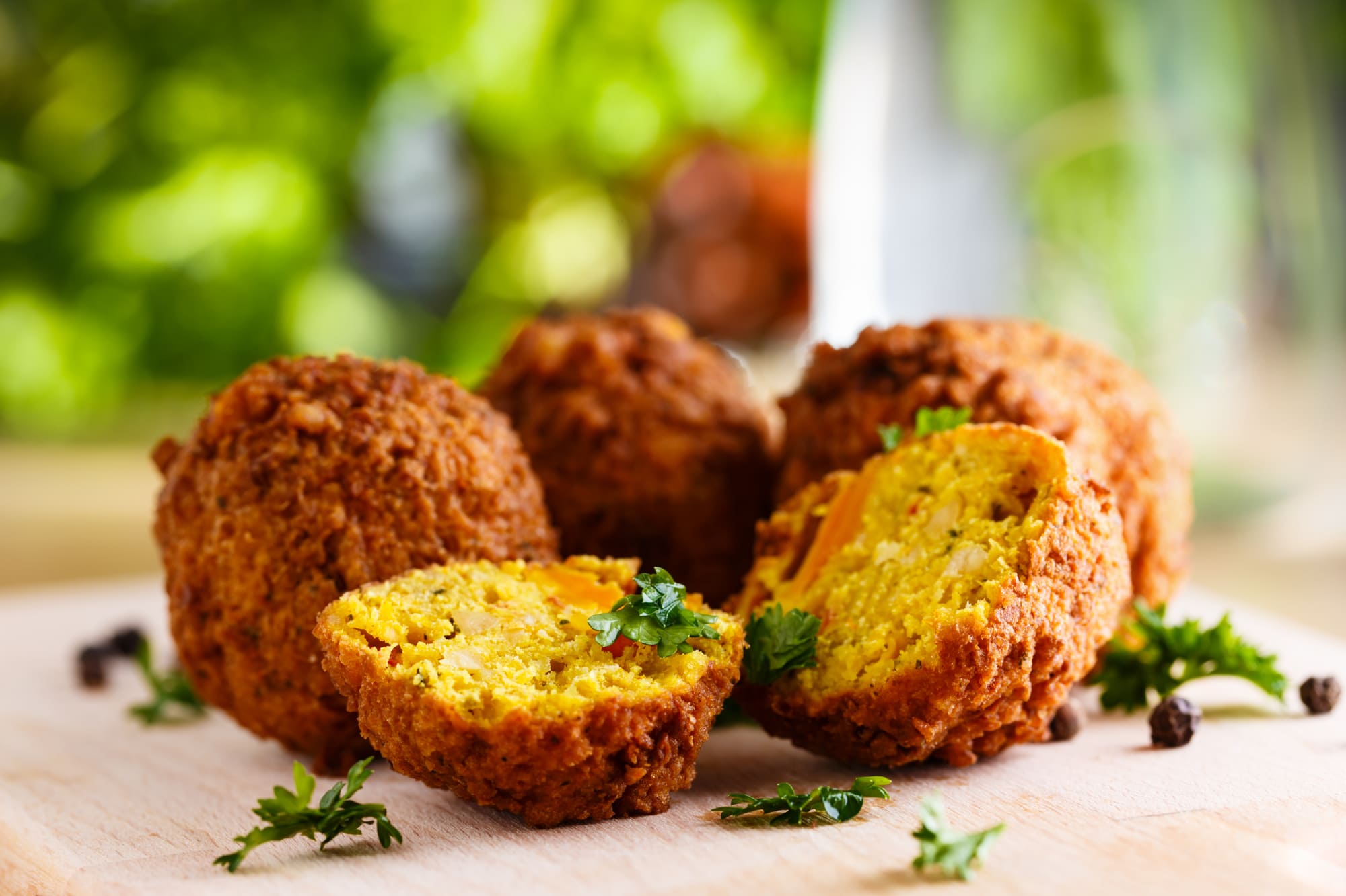 Vier knusprige Falafelbällchen, eines aufgeschnitten, garniert mit frischer Petersilie auf einer Holzoberfläche.